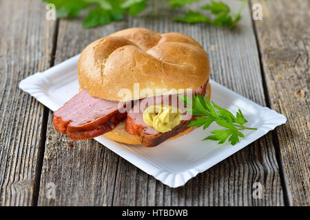 Bayerischen Speisen zum mitnehmen: eine Rolle mit gebackenen Leberkäse und Senf auf einem Pappteller Stockfoto