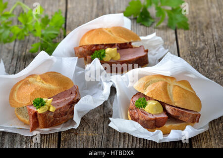 Bayerischen Speisen zum mitnehmen: drei Rollen mit gebackenen Leberkäse und Senf auf Packpapier mit einer Serviette Stockfoto