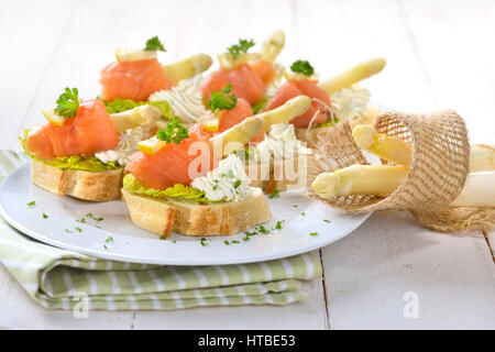 Köstliche Kanapees mit deutschen weißen Spargel, Sahne Käse mit Kräutern, verlässt Räucherlachs auf italienische Ciabatta-Brot mit Salat Stockfoto