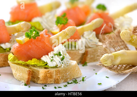 Köstliche Kanapees mit deutschen weißen Spargel, Sahne Käse mit Kräutern, verlässt Räucherlachs auf italienische Ciabatta-Brot mit Salat Stockfoto