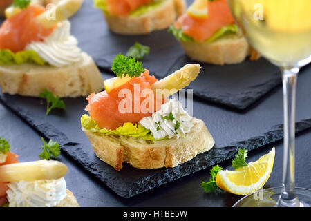 Köstliche Häppchen mit deutschen weißen Spargel, Frischkäse mit Kräutern, geräucherter Lachs auf italienisches Brot mit Salatblättern, serviert auf Schiefer Platten Stockfoto