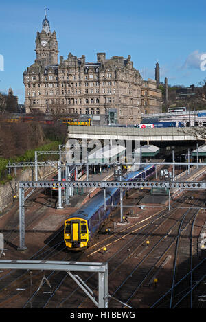 Ein Zug fährt Waverley Station in Edinburgh, im Hintergrund ist das Balmoral Hotel. Stockfoto