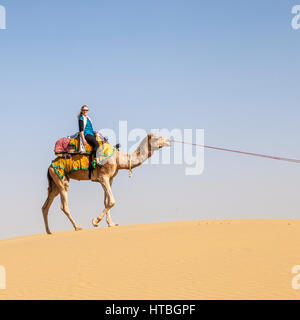 Eine Frau, ein Kamel reiten auf einer Sanddüne in der Wüste Thar, Rajasthan, Indien. Stockfoto