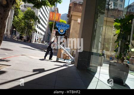 Im Stadtteil Financial District von San Francisco, Kalifornien schiebt ein Fedex-Zusteller einen Wagen beladen mit Parzellen in Richtung zum Eingang von einem Glas ummauerten Bürogebäude, 26. September 2016. Stockfoto