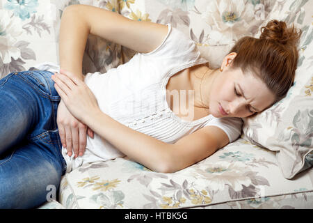 Junge schöne Mädchen mit Bauchschmerzen auf dem Sofa. Stockfoto