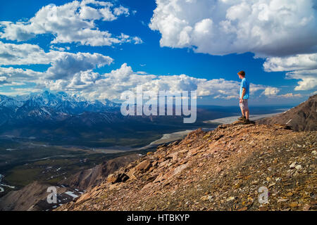 Ein Wanderer steht auf einem Felsvorsprung mit Blick auf das Delta Flusstal in einem Gebiet von der Alaska Range bekannt wie die Delta-Berge Stockfoto