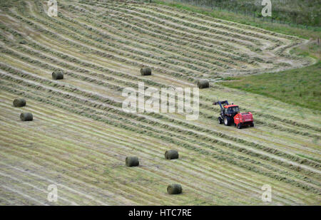 Ariel Ansicht von Farmer im roten Traktor Rettung Heu für den Einsatz als Silage (Feed) für sein Vieh in den schottischen Highlands, Schottland, Großbritannien. Stockfoto