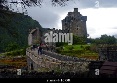 Touristen zu Fuß auf die Brücke zum Eilean Donan Castle auf der Road to the Isles in den schottischen Highlands. Stockfoto