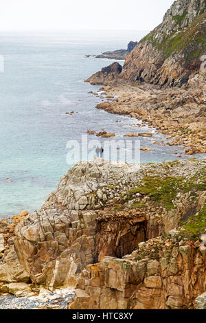 Ein Mann und eine Frau, die auf den Felsen am Ende des Tals Kinderbett befindet sich eine halbe Meile südlich von St Just in West Cornwall, England, Vereinigtes Königreich Stockfoto