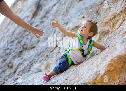 Kleines Mädchen in Kletterausrüstung streckte die Hand Mutter Stockfoto