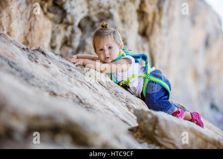 Kleines Mädchen in Sicherheitsgurt Klettern auf Felsen Stockfoto