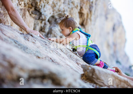 Kleines Mädchen in Sicherheitsgurt Klettern auf Felsen, Mama und Papa, die ihr von oben und unter Wahrung Stockfoto