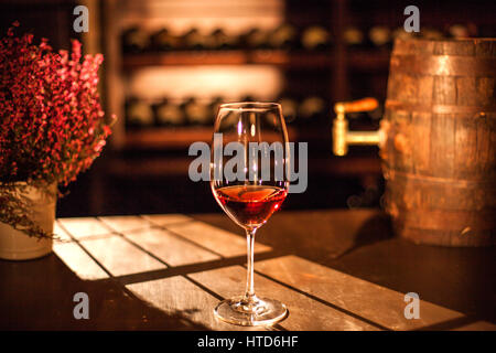 Glas Wein auf den Holztisch neben Blumen und kleine hölzerne Weinfass gelegt. Stockfoto