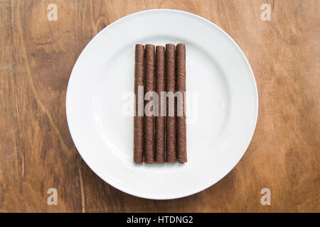 Wafer rollt mit Schokolade in weißer Teller auf Holztisch. Stockfoto