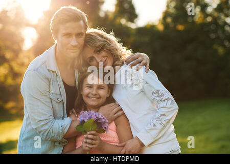 Porträt eines lächelnden Mädchens halten einen Blumenstrauß und genießen Sie einen sonnigen Nachmittag in einem Park mit ihrer Mutter und Vater Stockfoto