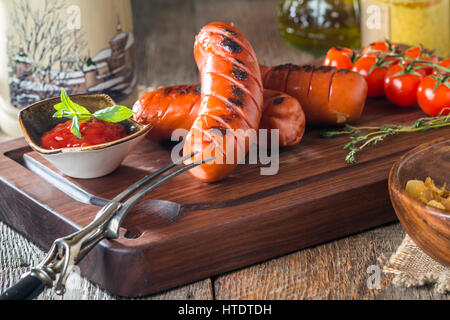 Gegrillte Würstchen mit Kraut, Tomaten und Glas Bier auf Holzbrett Stockfoto