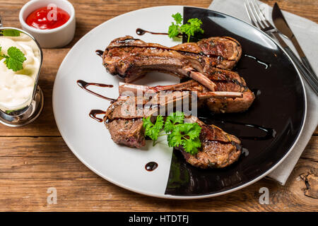 Luxus-Dinner serviert Gegrilltes Lamm Rippen mit Sauce auf Teller auf hölzernen Hintergrund Stockfoto