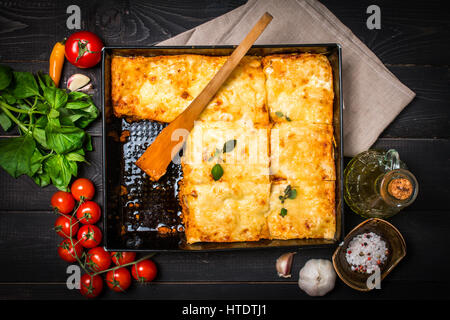 Köstliche traditionelle italienische Lasagne mit Zutaten serviert auf dunkel rustikalen Holztisch, Ansicht von oben Stockfoto