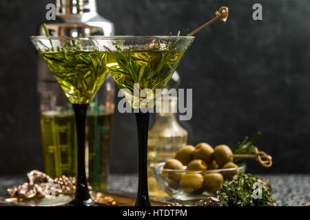 Zwei frische grüne Cocktails mit Rosmarin und Oliven in Martini-Gläser auf grauem Hintergrund Stockfoto