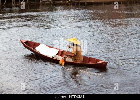 Ein asiatischer Mann seine kleine Ruderboot mit einem kleinen Paddel auf einem braunen farbigen Flussufer am Nachmittag Singkawang. Stockfoto