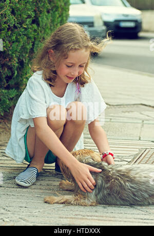 Niedliche kleine Mädchen mit streunenden Hund auf der Straße. Stockfoto