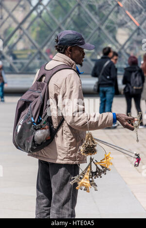 Paris, Frankreich. Eine Hausierer verkauft Selfie-Sticks und Modelle der Eifelturm in der Nähe von Eingang zum Louvre-Museum und den berühmten Glaspyramide. Stockfoto