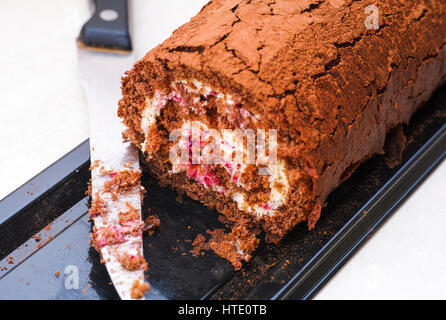 Teil der leckeren Schokolade Biskuit roll mit Sahne und Messer auf schwarzen Plastikschale. Stockfoto