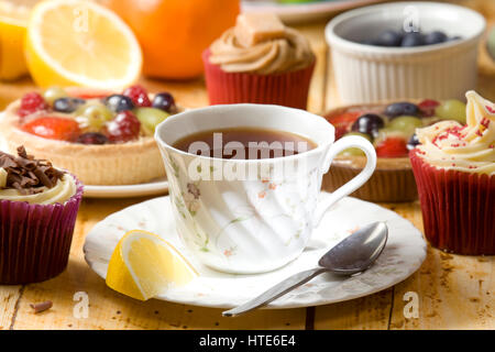 schwarzer Tee und Zitrone mit Muffins und Kuchen im Hintergrund Stockfoto