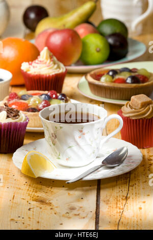 schwarzer Tee mit einem Stück Zitrone und Kuchen im Hintergrund Stockfoto