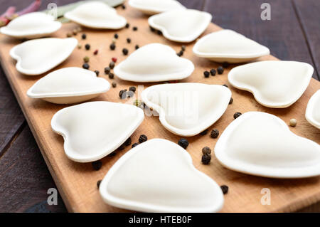 Rohen Teig in der Form eines Herzens (Knödel, Ravioli, Pelmeni), auf ein Schneidebrett. Nahaufnahme Stockfoto