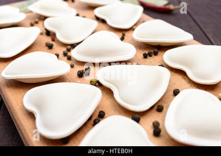 Rohen Teig in der Form eines Herzens (Knödel, Ravioli, Pelmeni), auf ein Schneidebrett. Nahaufnahme Stockfoto