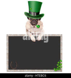 schöne süße Mops Welpen Hund mit Kobold Hut für St. Patricks Day Pfeife, stützte sich auf leere Tafel Schild mit Hufeisen und Kleeblatt, isolat Stockfoto
