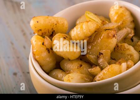 Horizontale Foto von gekochten und gebratenen Gnocchi in zwei Schüsseln als Teil des Hauses platziert. Essen ist zusammen mit gerösteten Zwiebeln serviert. Alles liegt auf vinta Stockfoto