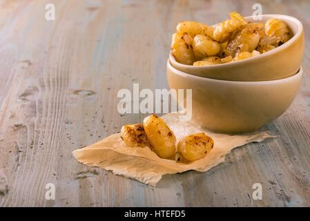 Horizontale Foto von gekocht und gebraten Gnocchi auf Blatt Papier vor zwei Schüsseln mit Teil des Hauses. Einige Stücke werden zusammen mit Roas serviert. Stockfoto