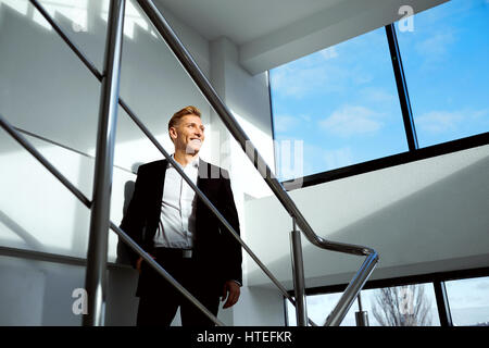 Ein blonder Mann schaut aus dem Fenster bei der Landung im Bürogebäude. Stockfoto