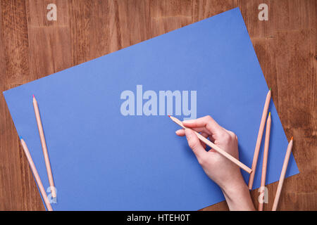 Mädchen Hand zeichnen, leere blaue Papier und bunte Bleistifte auf Holztisch. Kreatives Konzept. Kunst und Design. Künstler. Zeichnen und malen. Stockfoto