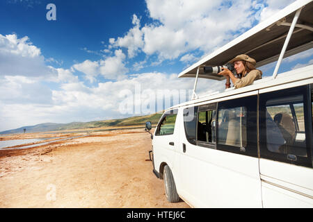 Junge Frau im offenen Dach des Safari Kleinbus stehen und Fotografieren der afrikanischen Savanne Stockfoto