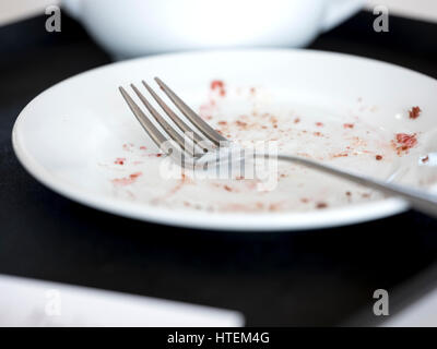 Eine gebrauchte Gabel, die auf einem leeren Teller mit Krümel neben einer Teeschale liegt. Stockfoto