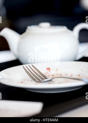 Eine gebrauchte Gabel, die auf einem leeren Teller mit Krümel neben einer Teeschale liegt. Stockfoto