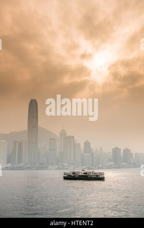 Mit der Fähre in den Victoria Harbour mit den Wolkenkratzern und die Skyline von Hong Kong, mit der Sonne durch dramatische Wolken. China. Stockfoto