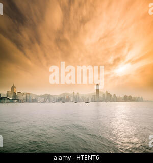 Mit der Fähre in den Victoria Harbour mit den Wolkenkratzern und die Skyline von Hong Kong, mit der Sonne durch dramatische Wolken. China. Stockfoto