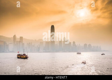 Mit der Fähre in den Victoria Harbour mit den Wolkenkratzern und die Skyline von Hong Kong, mit der Sonne durch dramatische Wolken. China. Stockfoto