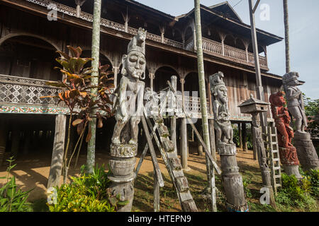 Patong oder Holz geschnitzte Bildnisse stehen neben einem Lamin oder Langhaus Eingang mit Holz geschnitzten Schritten erstellt aus einem einzigen Stück Bornean Ironwood (Kayu Stockfoto