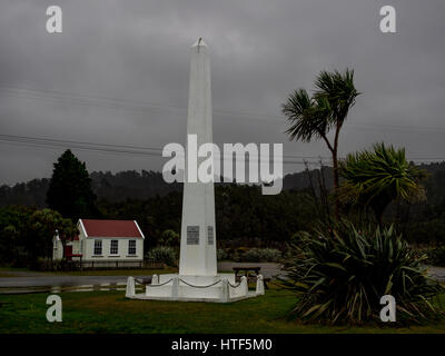 Tasman Denkmal mit historischen Schulhaus hinter Okarito, South Westland, Neuseeland. Einen düsteren Abend Kohl Baum Ti Kouka verlässt Schlag im Wind. Stockfoto