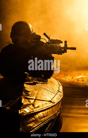 Beleuchtete Silhouette der Spezialeinheiten marine Betreiber in militärischen Kajak auf Feuer Explosion Hintergrund. Schlacht-Betrieb Stockfoto