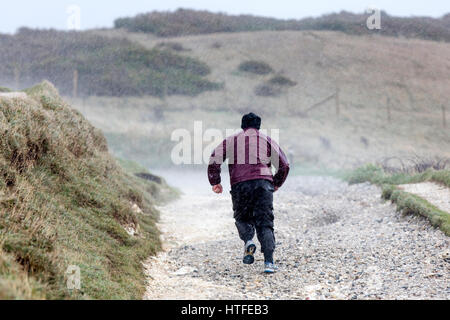 Ein Mann läuft joggt entlang einer Küstenweg von einem heftigen Sturm ertappt. Es regnet hart und seinem Kit ist klatschnass, wie er seinen Weg auf einem Hügel macht