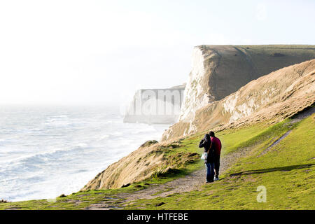 Menschen stehen auf der Dorset Jurassic Coast Path bei Durdle Door machen an einem windigen Nachmittag. Mann Frau Küste stürmischem Wetter Winter dor Stockfoto