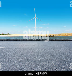 Windkraftanlagen in grüner Landschaft neben einer Straße gegen blauen Himmel, alternative Energien, neue Landschaft Stockfoto