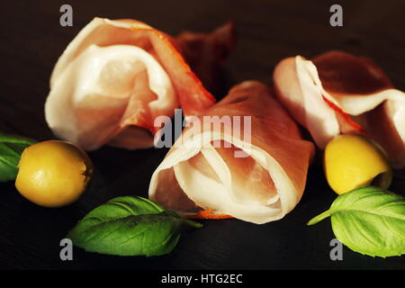 Gewellten Scheiben von Delicious Prosciutto mit Basilikum und Oliven auf Granit. Stockfoto