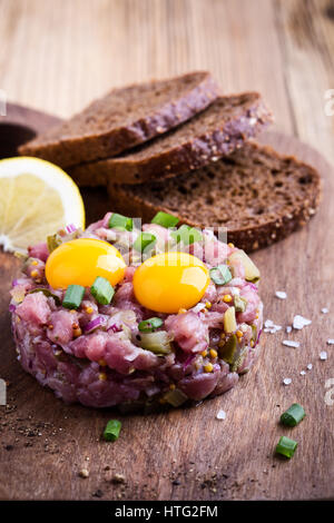 Steak Tartar in Ring-Form geformt, gekrönt mit zwei Wachteln Eigelb und mit Roggenbrot auf Holzbrett serviert Stockfoto